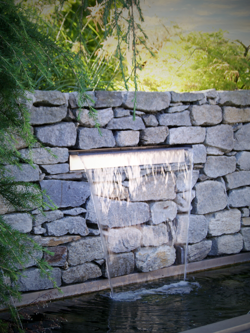 Dynamische Gartengestaltung Eder Steinmauer Steinmauer aus der ein Wasserfall in ein Auffangbecken fliesst.