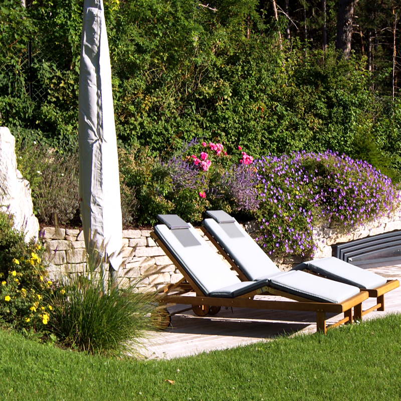 Dynamische Gartengestaltung Eder Gartenanlage 2 Holzliegestühle in einer gepflegten Gartenlandschaft. Im Hintergrund eine Natursteinmauer als Abgrenzung.