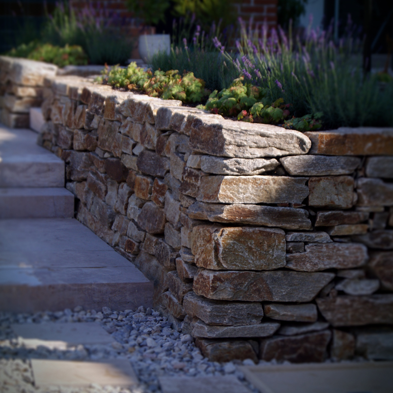 Gartengestaltung Eder Steinmauer Natursteinmauer als Hangbegrenzung mit Stauden bepflanzt